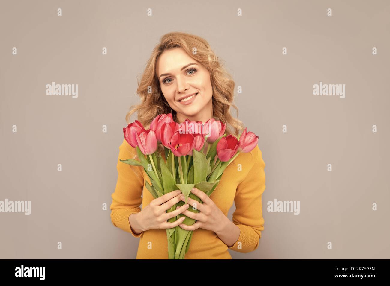 sorridente signora tenere fiori per le vacanze di primavera su sfondo grigio Foto Stock