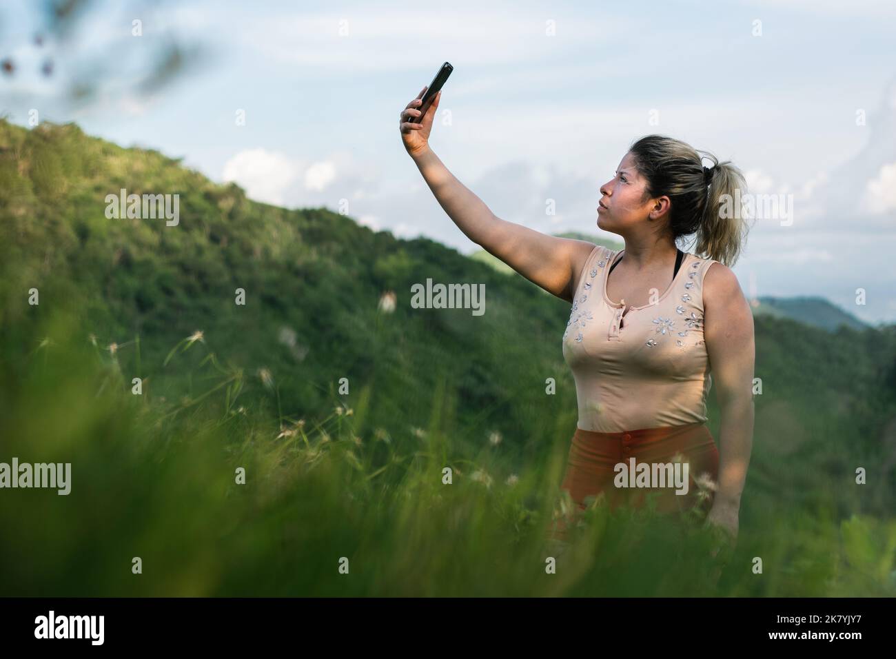 bella giovane donna latina, in cima ad una montagna in cerca di copertura di rete per il suo cellulare. ragazza in cerca di segnale satellitare, escursioni in cima o Foto Stock