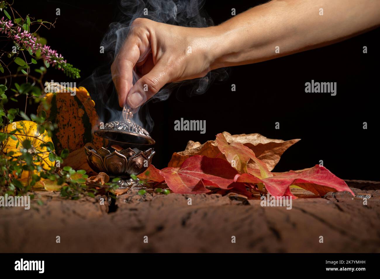 La mano di una donna mette il fuoco su un bastone di incenso su un bruciatore. Sfondo per la meditazione. Foto Stock