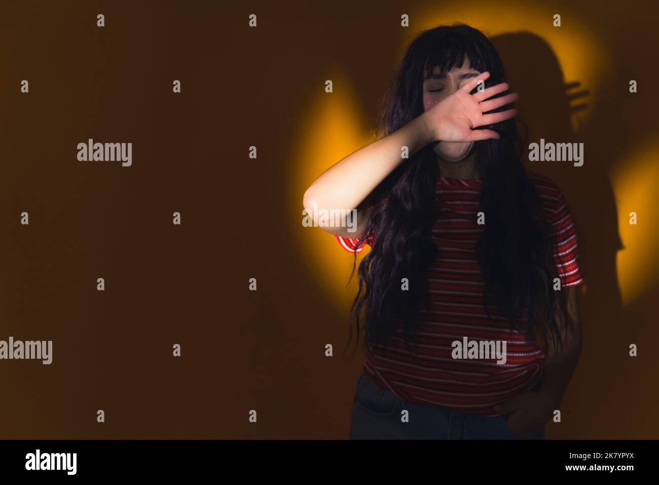 Una giovane, bella ragazza con lunghi capelli scuri appoggiati al muro al centro della luce circolare, nascondendo il viso con il braccio. Foto di alta qualità Foto Stock