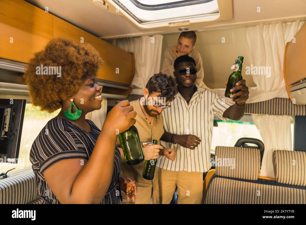 Gruppo interrazziale di amici-viaggiatori che ballano nel salotto del furgone, tenendo bottiglie di vetro verde pieno di birra gustosa, e ridendo. I Millennial a una festa. Foto di alta qualità Foto Stock