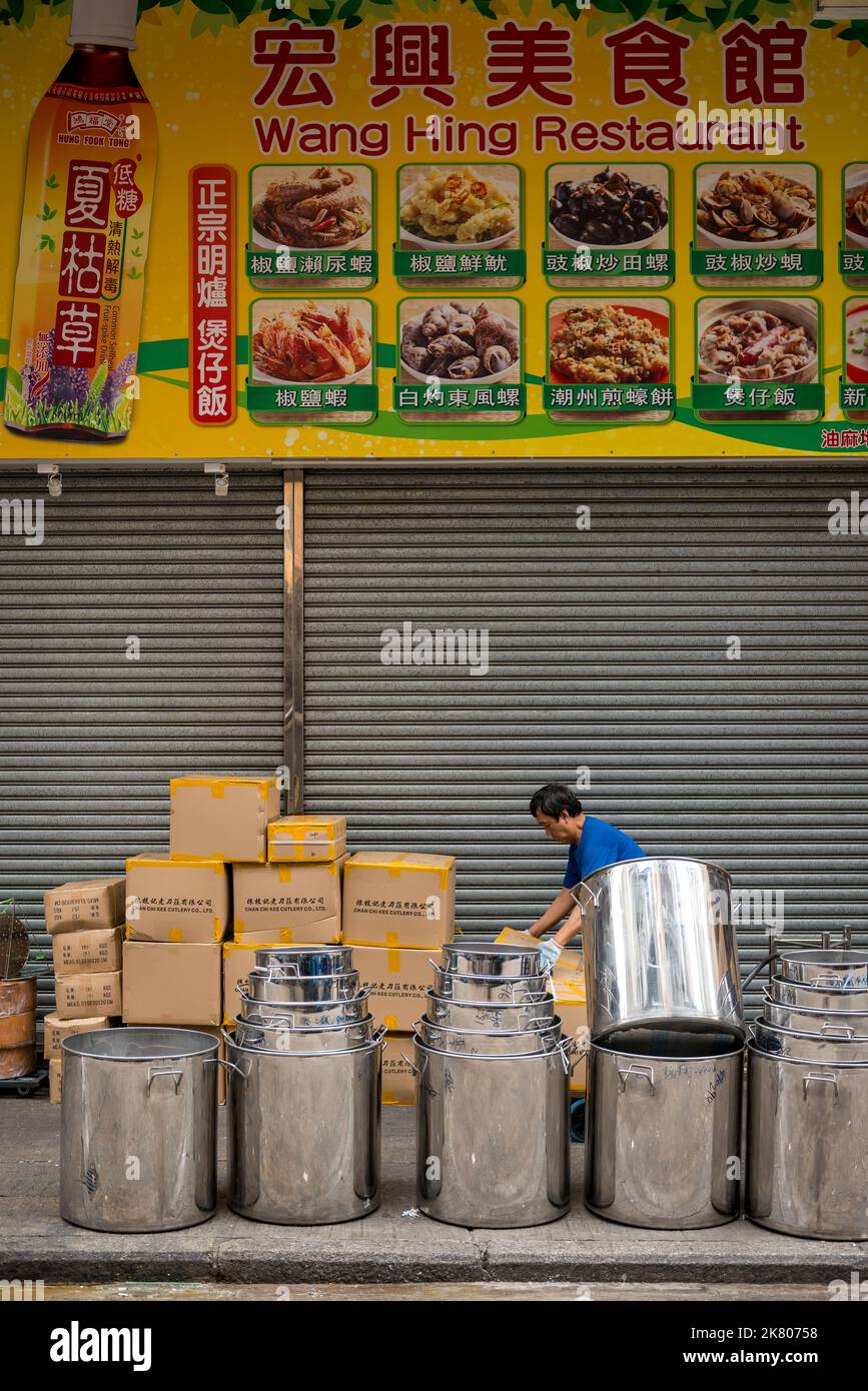 Un uomo impila scatole di utensili da cucina e grandi pentole di acciaio al di fuori di un ristorante chiuso, Temple Street, Yau ma Tei, Kowloon, Hong Kong Foto Stock