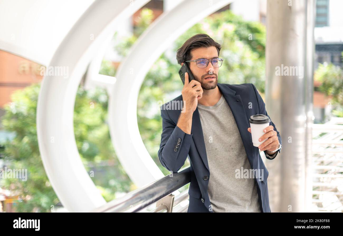 L'uomo che tiene una tazza di caffè e usa uno smartphone e parla con l'amico mentre aspetta il suo amico in aeroporto. Foto Stock