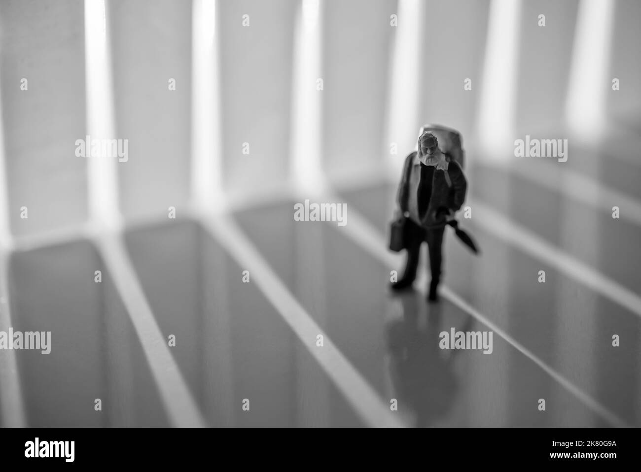 Mini persone giocattoli allestito studio - un vecchio uomo con zaino e ombrello a piedi durante l'alba o il tramonto. Il rumore è stato aggiunto per un effetto straordinario. Foto Stock