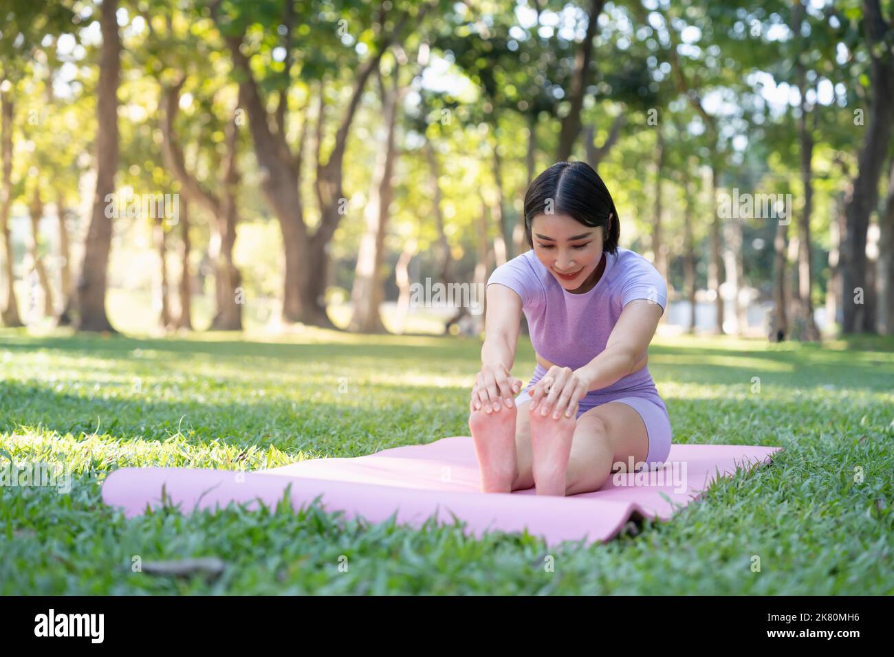 Attraente giovane donna asiatica pratica yoga, esercizio nel parco, in piedi una gamba su un materassino yoga, mostrando una postura di equilibrio. Stile di vita benessere e. Foto Stock