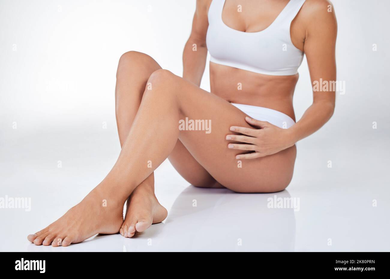 Il corpo è una macchina e ha bisogno di manutenzione. Una donna seduta sul pavimento che tocca le gambe contro lo sfondo di uno studio. Foto Stock