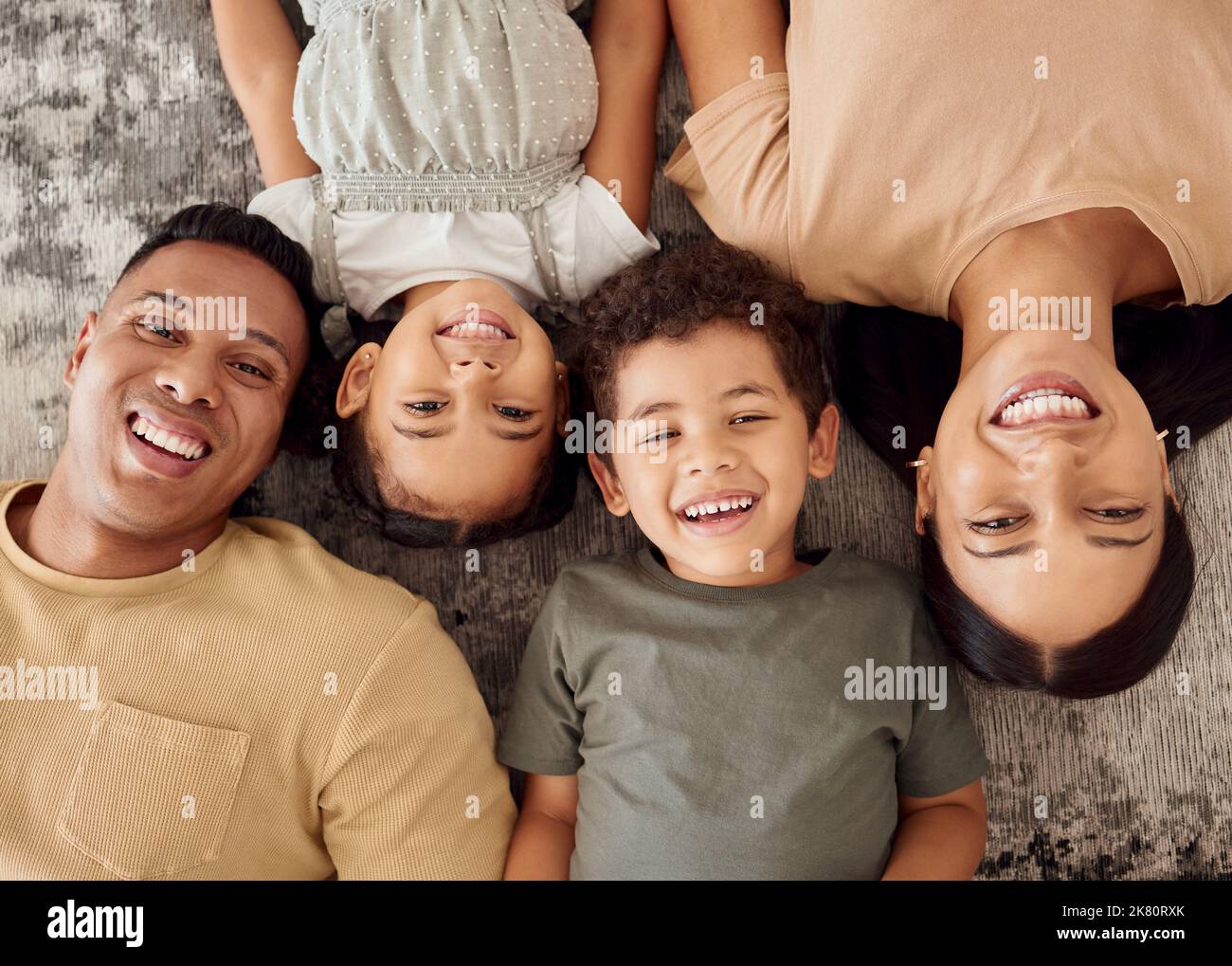 I bambini, i genitori e sdraiati sul pavimento dall'alto, la felicità che passa il tempo insieme nella casa della famiglia. Mamma, papà e bambini sorridenti sul tappeto, felici Foto Stock