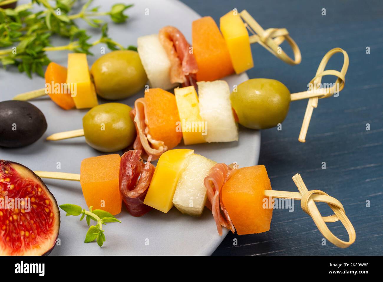 Spiedini con formaggio, olive e jamon su piatto grigio. Primo piano. Sfondo blu. Foto Stock