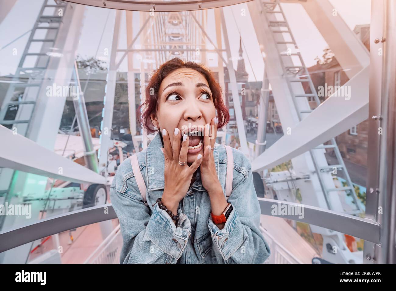 La ragazza impaurita nella ruota panoramica sta sperimentando un attacco di panico dovuto alla paura delle altezze. Il giro si è rotto e si è bloccato. Fobie psicologiche e pr Foto Stock