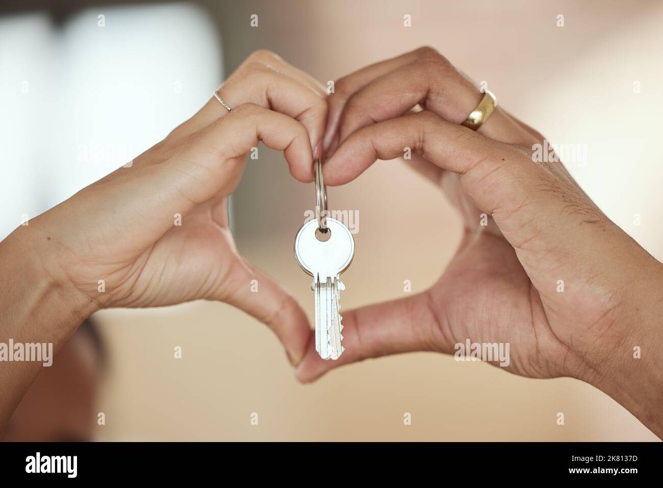 Una casa è costruita sull'amore, una giovane coppia che forma un cuore intorno alle chiavi della loro casa con le mani. Foto Stock