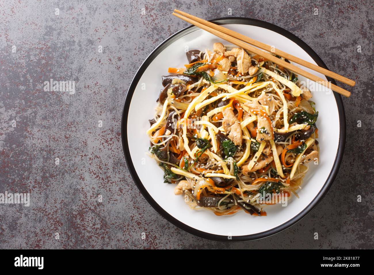 Cibo coreano fritto con spaghetti, carne, funghi e verdure chiamato Japchae closeup sul piatto sul tavolo. Vista orizzontale dall'alto Foto Stock