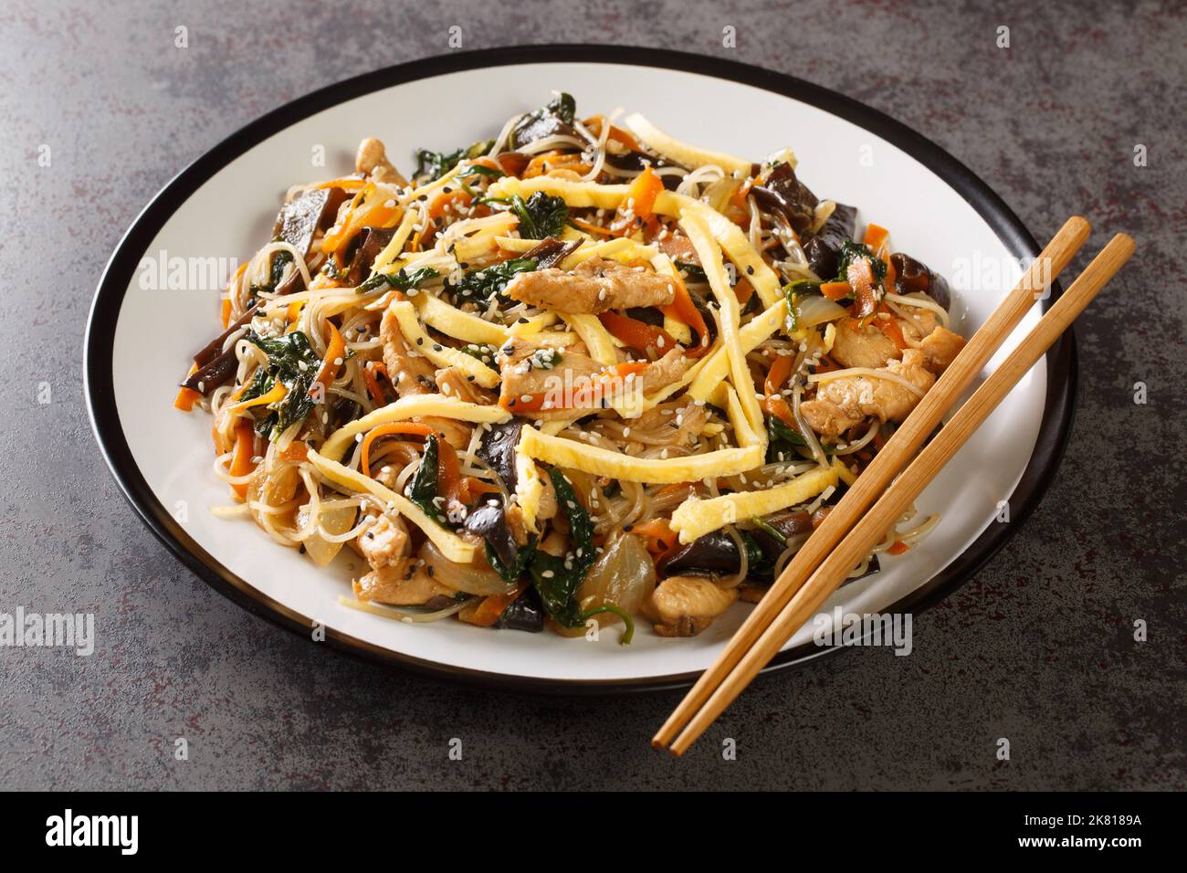 Japchae cibo coreano con carne, uova, vermicelli e verdure primo piano sul piatto sul tavolo. Orizzontale Foto Stock