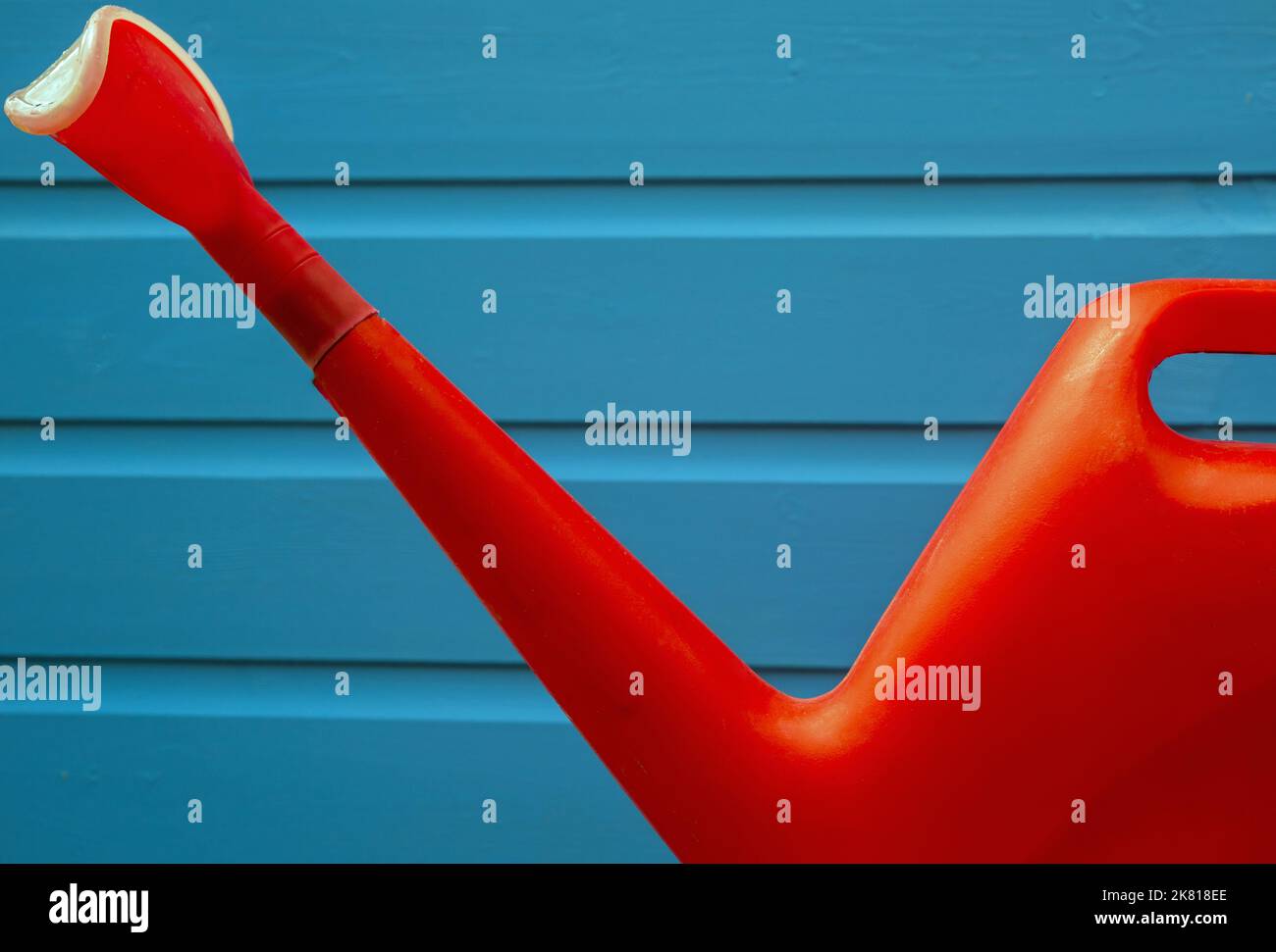 Un'annaffiatura di plastica rossa brillante su uno sfondo blu Foto Stock