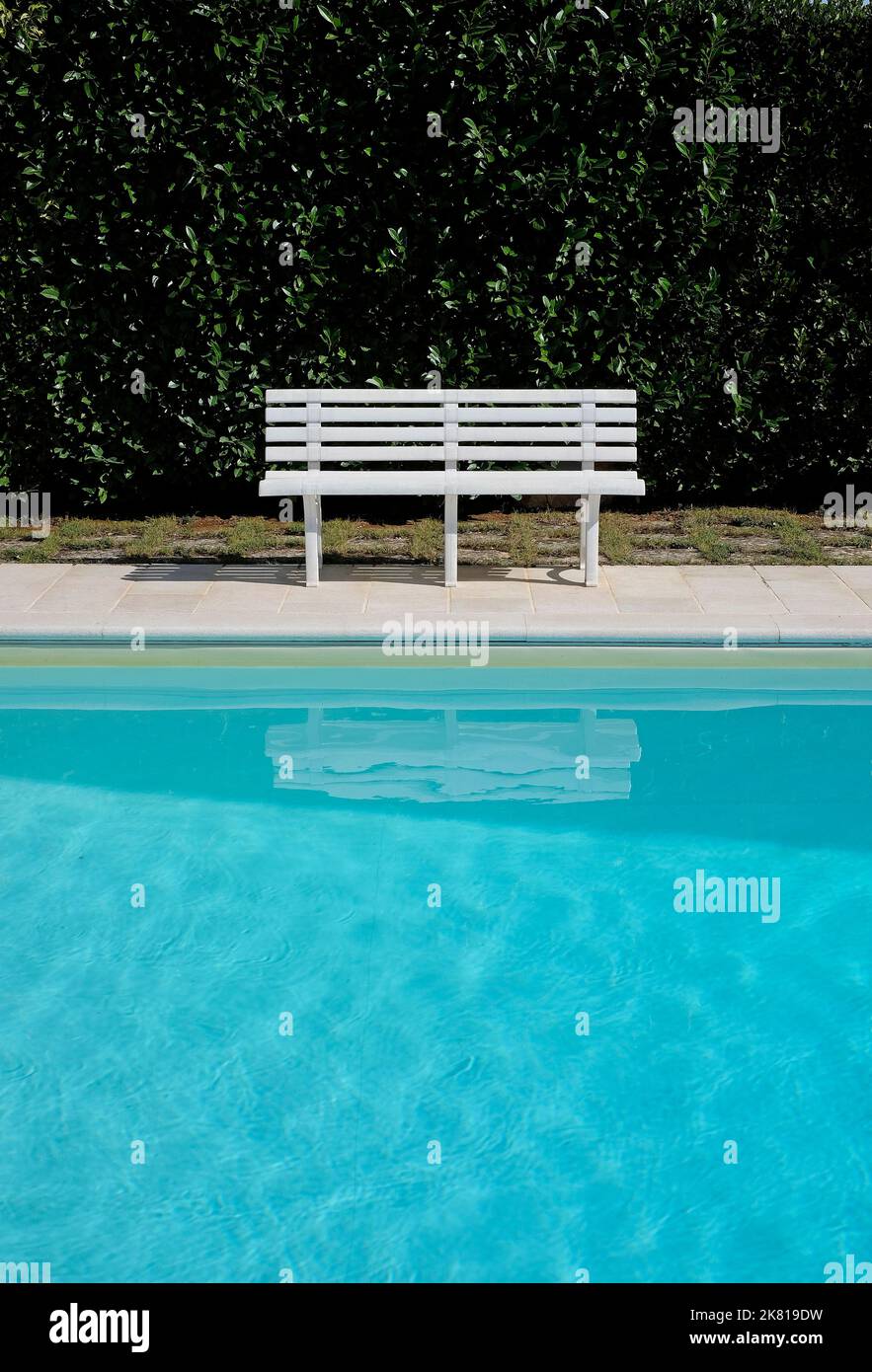 sedile a panca bianco vicino alla piscina blu con fondo di siepe Foto Stock