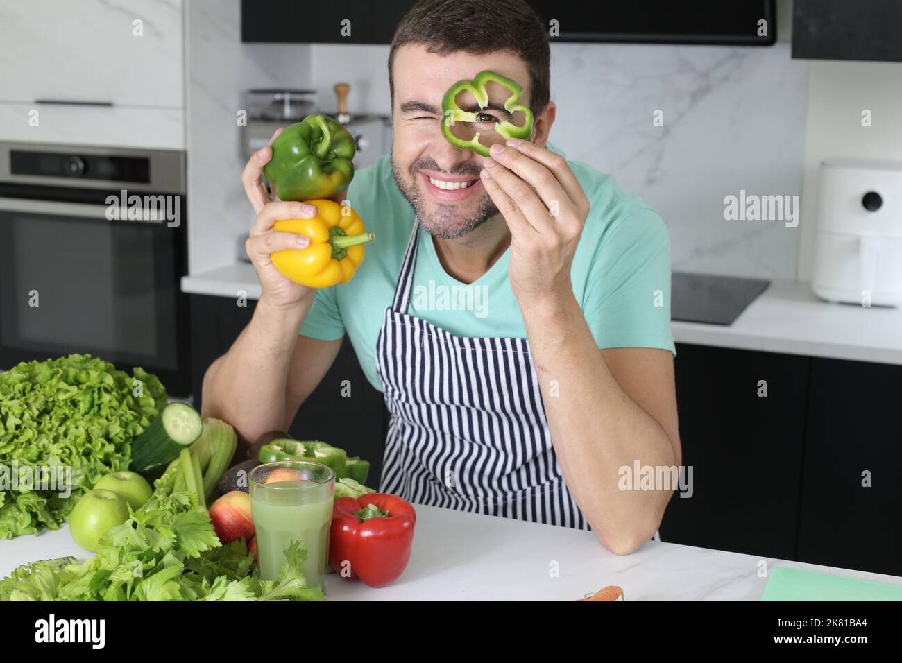 Uomo che gioca con peperoni verdi in cucina Foto Stock