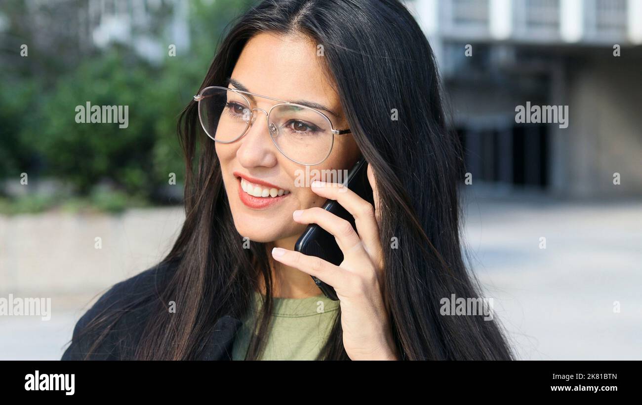 Primo piano di una donna di affari latina sorridente con gli occhiali che parlano sul telefono delle cellule. Foto Stock