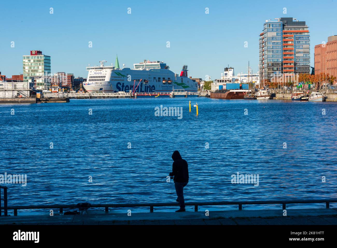 Kieler Hafen bei herrlichem, Sonnenschein ein Angler fängt Fische, im Hintergrund die Schwedenfähre nach Göteborg Foto Stock