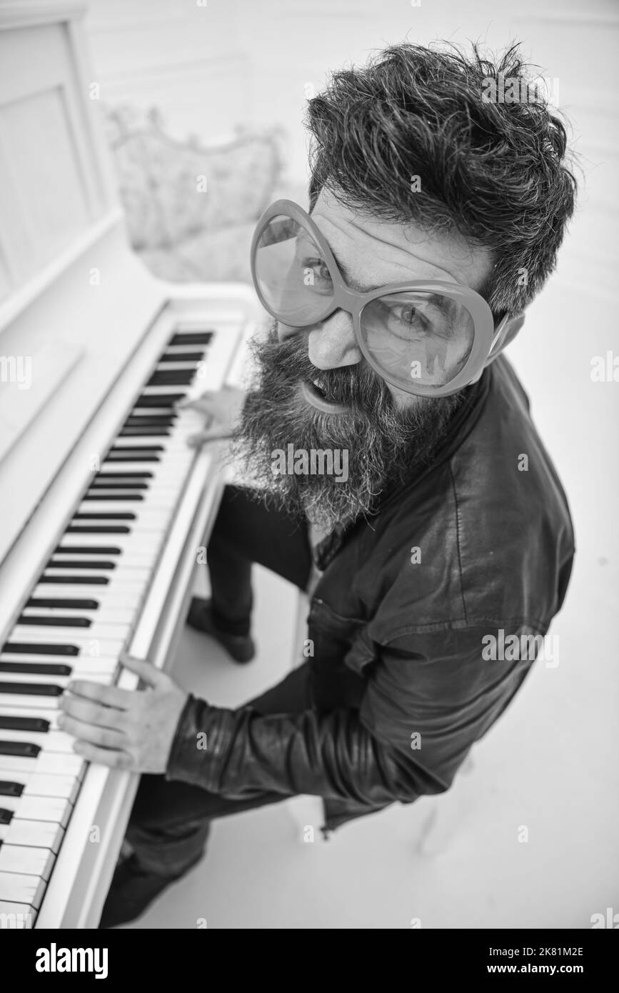 Ragazzo in giganteschi occhiali da sole rossi mentre suona il pianoforte. Uomo, allegro pianista che suona. Concetto di comic performer. L'uomo in giacca di pelle si siede vicino al piano musicale Foto Stock