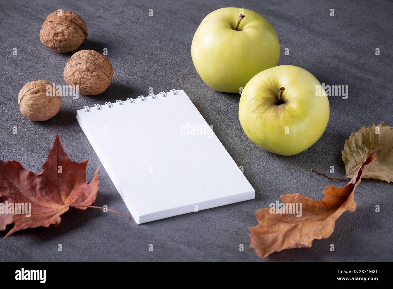 Composizione autunnale di foglie secche, mele, noci bianco blocco note. Foto Stock
