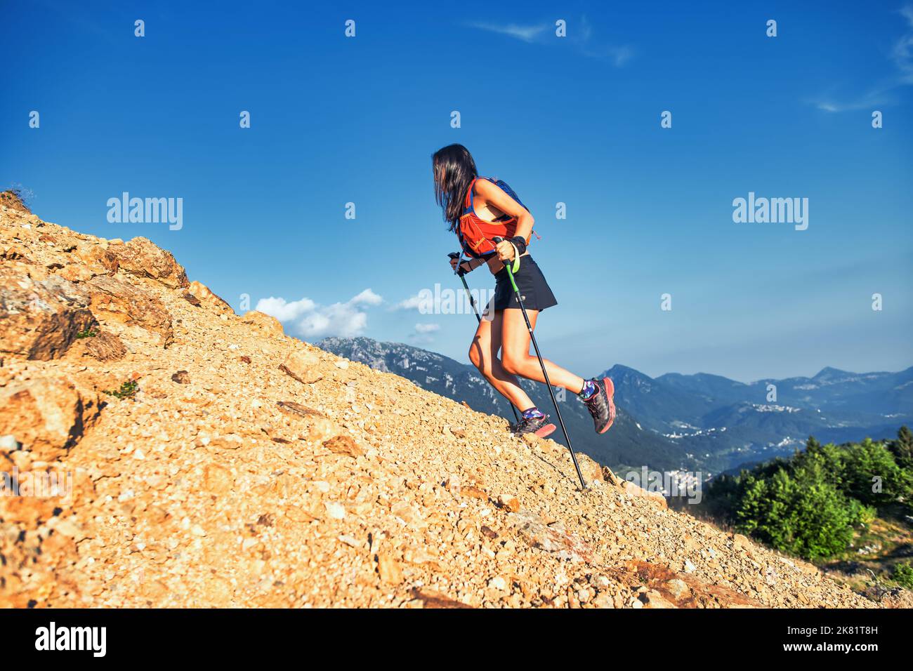 Donna sale un pendio roccioso in montagna con pali Foto Stock