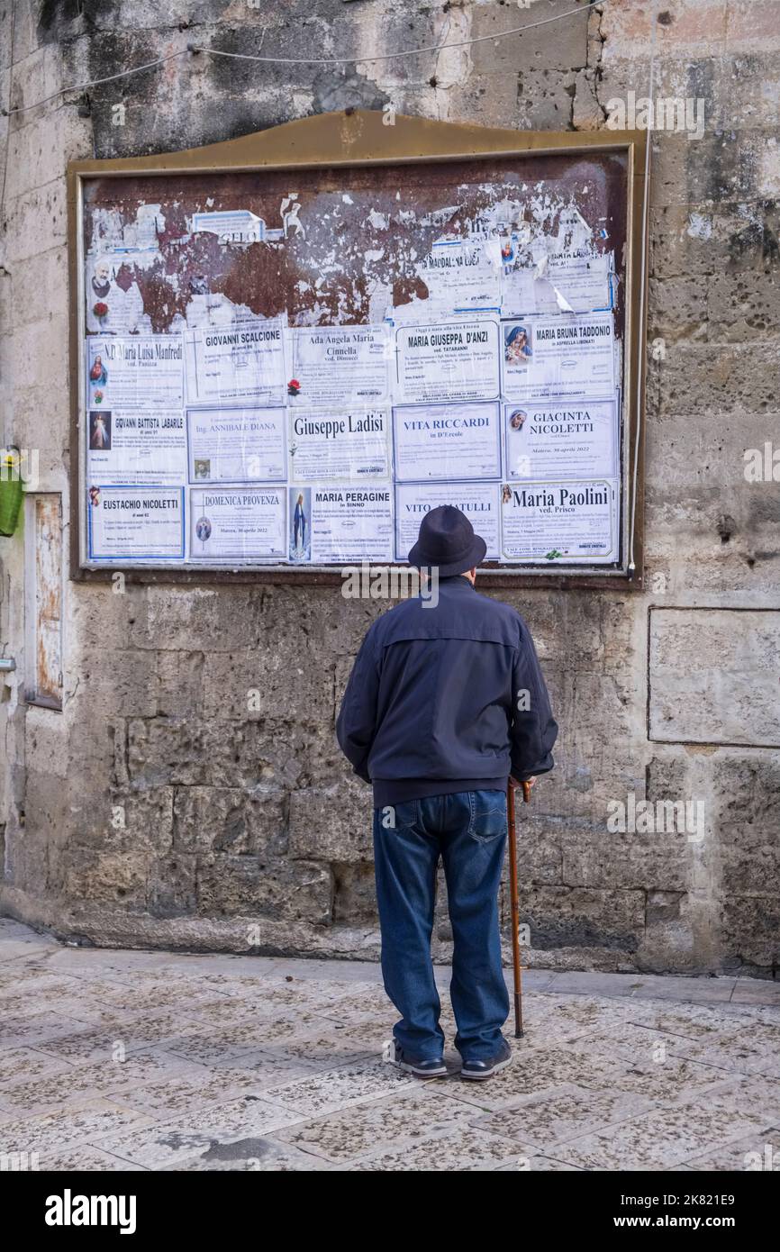 Italia, Basilicata regione: Matera. Uomo che guarda un cartello di avviso di morte in Piazza Vittorio Veneto. La città è dichiarata patrimonio mondiale dell'UNESCO SIT Foto Stock