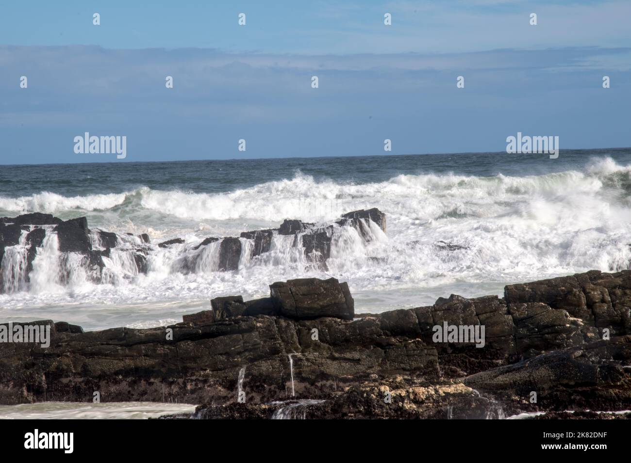 Onde che si infrangono contro rocce che si infrangono sulla costa Foto Stock