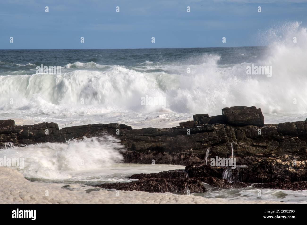 Onde che si infrangono contro rocce che si infrangono sulla costa Foto Stock
