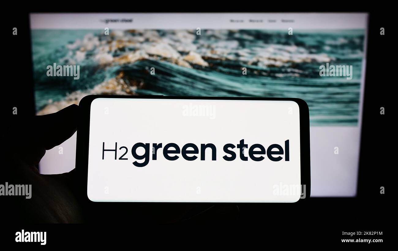 Persona che tiene il cellulare con il logo della società svedese di idrogeno H2 Green Steel sullo schermo di fronte al sito web aziendale. Messa a fuoco sul display del telefono. Foto Stock