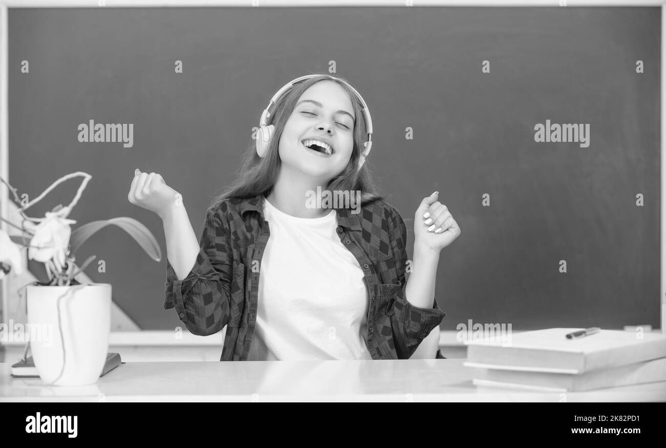 la ragazza felice tiene le cuffie moderne nella high school alla lavagna, infanzia Foto Stock