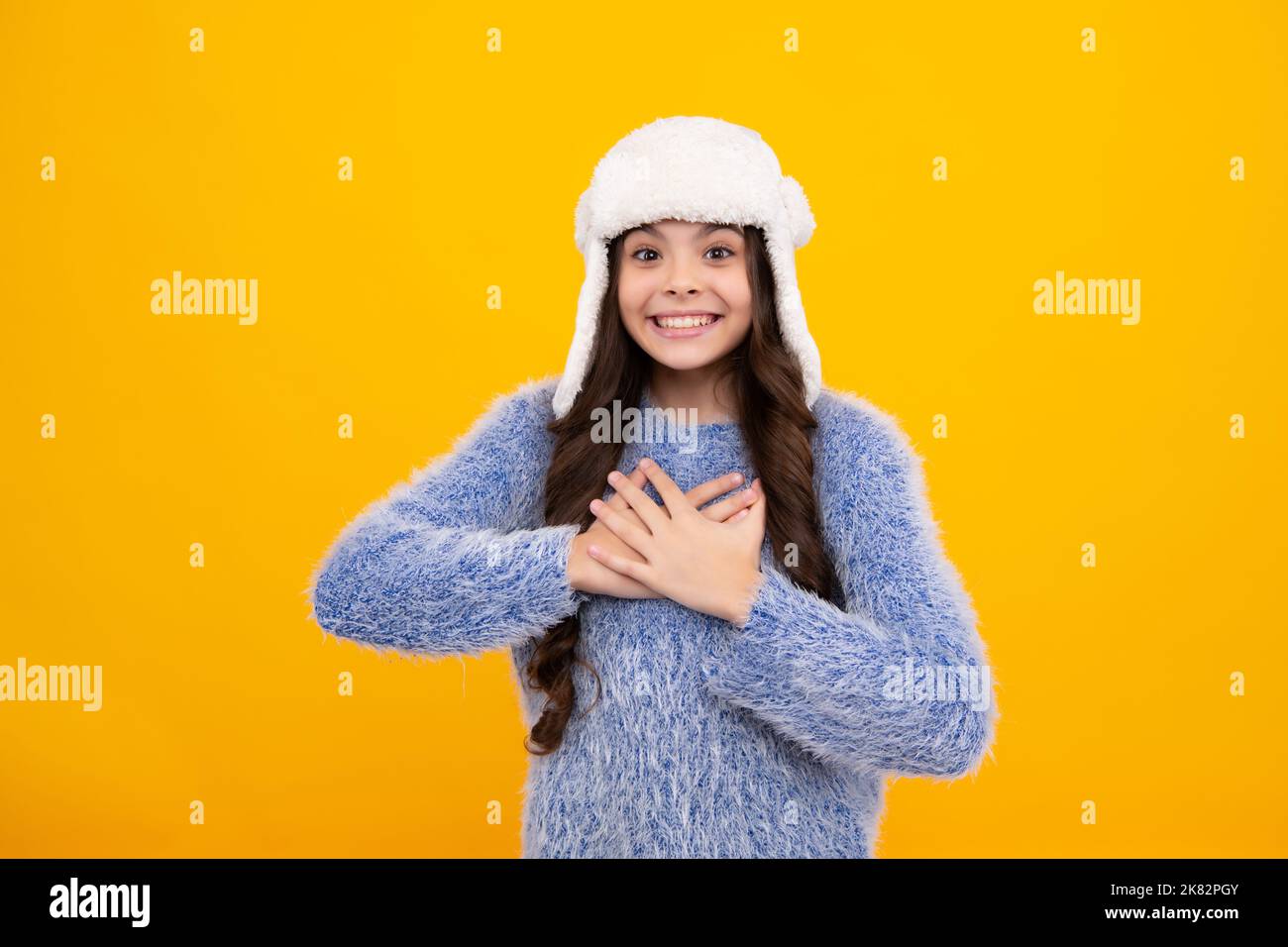 Bel ritratto invernale per bambini. Ragazza adolescente in posa con maglione invernale e cappello a maglia su sfondo giallo. Felice adolescente, positivo e sorridente Foto Stock