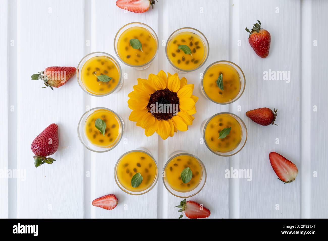cibo e carta da parati natura, tavolo decorato con un girasole e attorno ad esso bicchieri con frutto della passione dessert, antipasti gourmet in studio Foto Stock