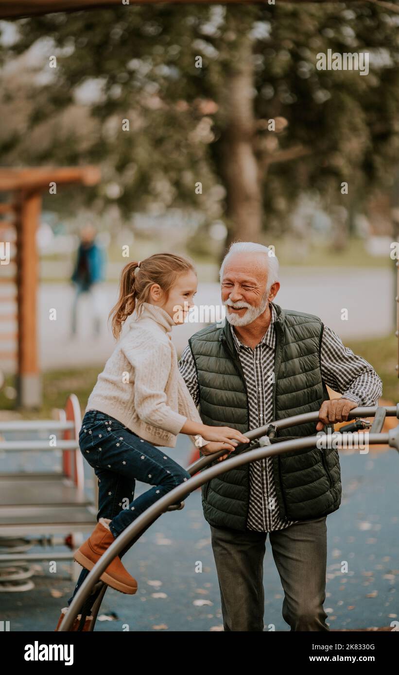 Bel nonno trascorrere del tempo con sua nipote nel parco giochi il giorno d'autunno Foto Stock