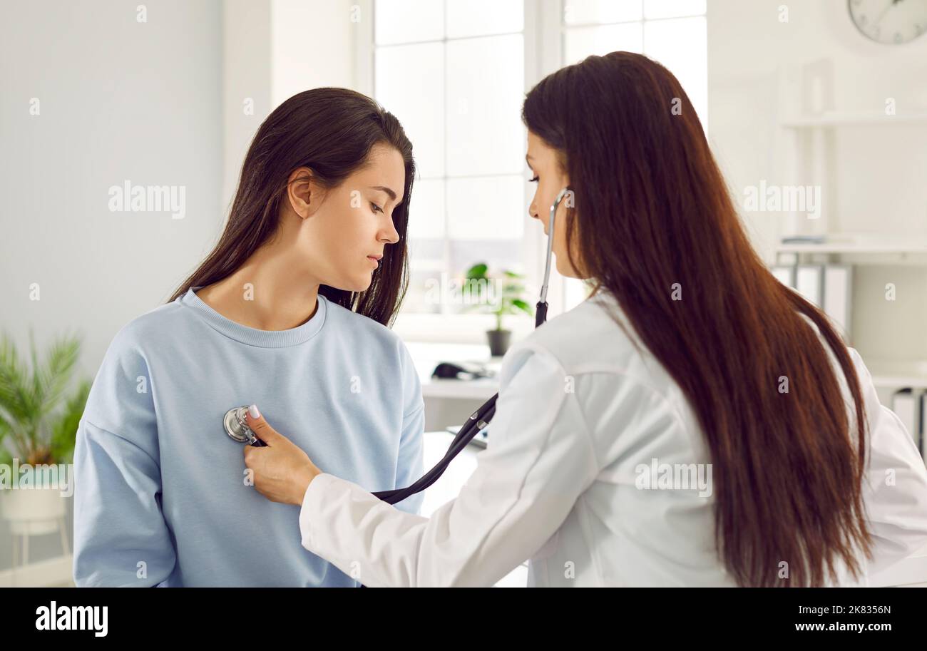 Giovane donna caucasica afflitta in esame in clinica privata siede medico di fronte con stetoscopio Foto Stock