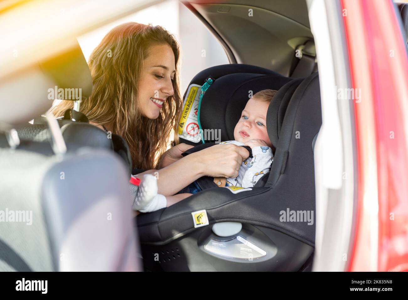 La madre allaccia il figlio nel sedile dell'auto e gli mette la cintura di sicurezza Foto Stock