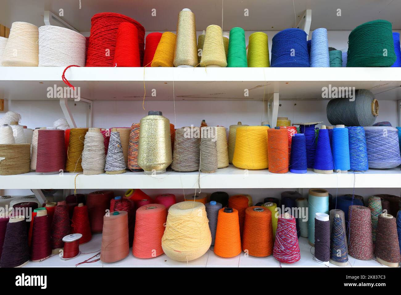 Coni e rocchetti di filo da cucire colorato organizzati per colore rosso, arancione, giallo, blu Foto Stock