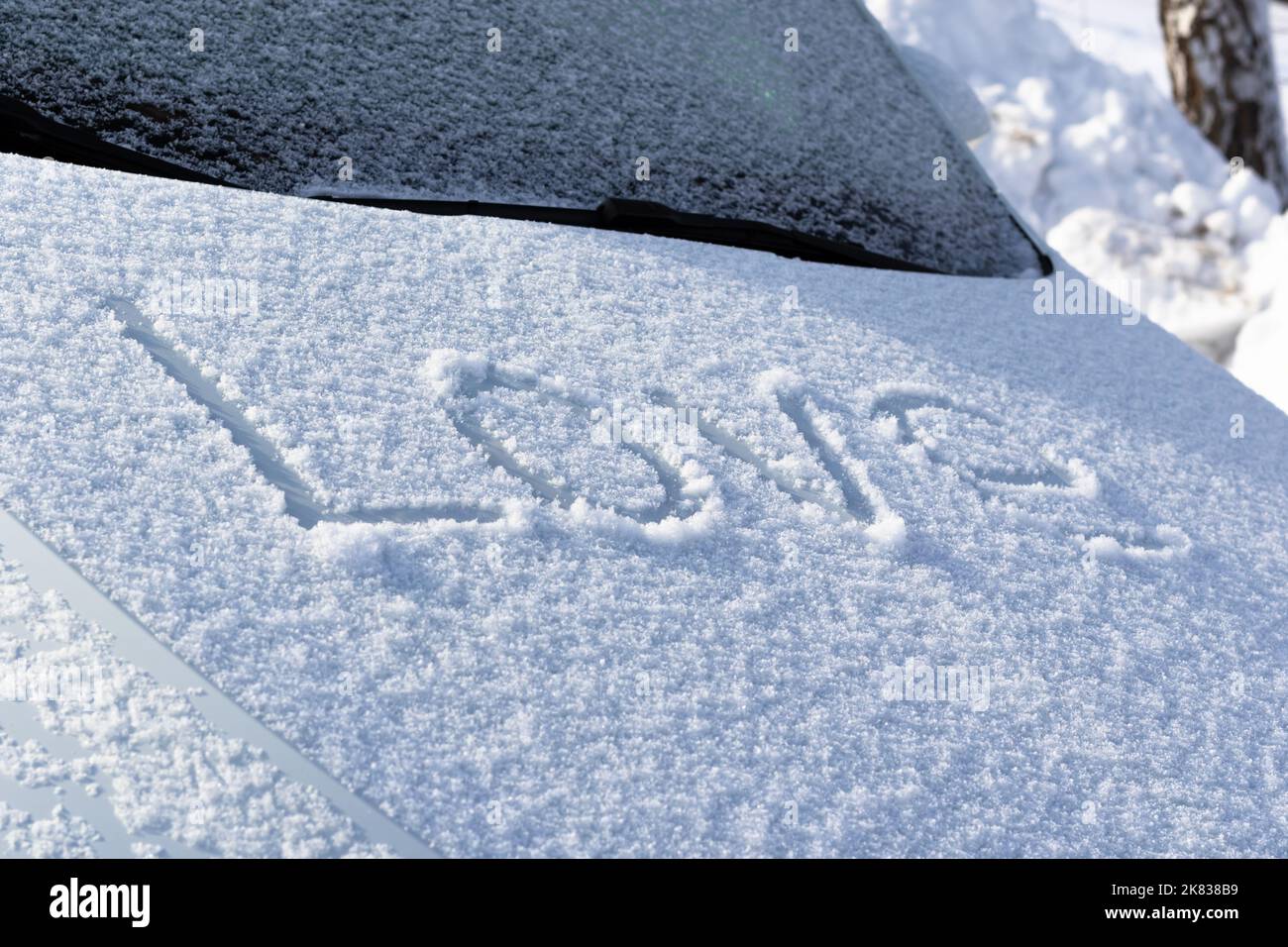 L'iscrizione sul cofano innevato della vettura in grandi lettere amore in una giornata invernale soleggiata. Messa a fuoco selettiva. Primo piano Foto Stock
