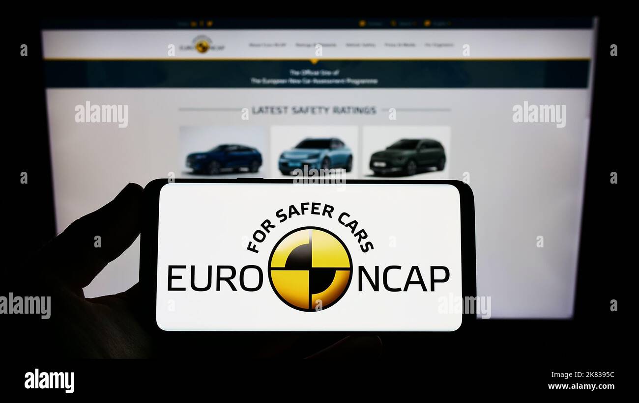 Persona che tiene uno smartphone con il logo del programma di sicurezza dell'auto Euro NCAP sullo schermo di fronte al sito Web. Messa a fuoco sul display del telefono. Foto Stock