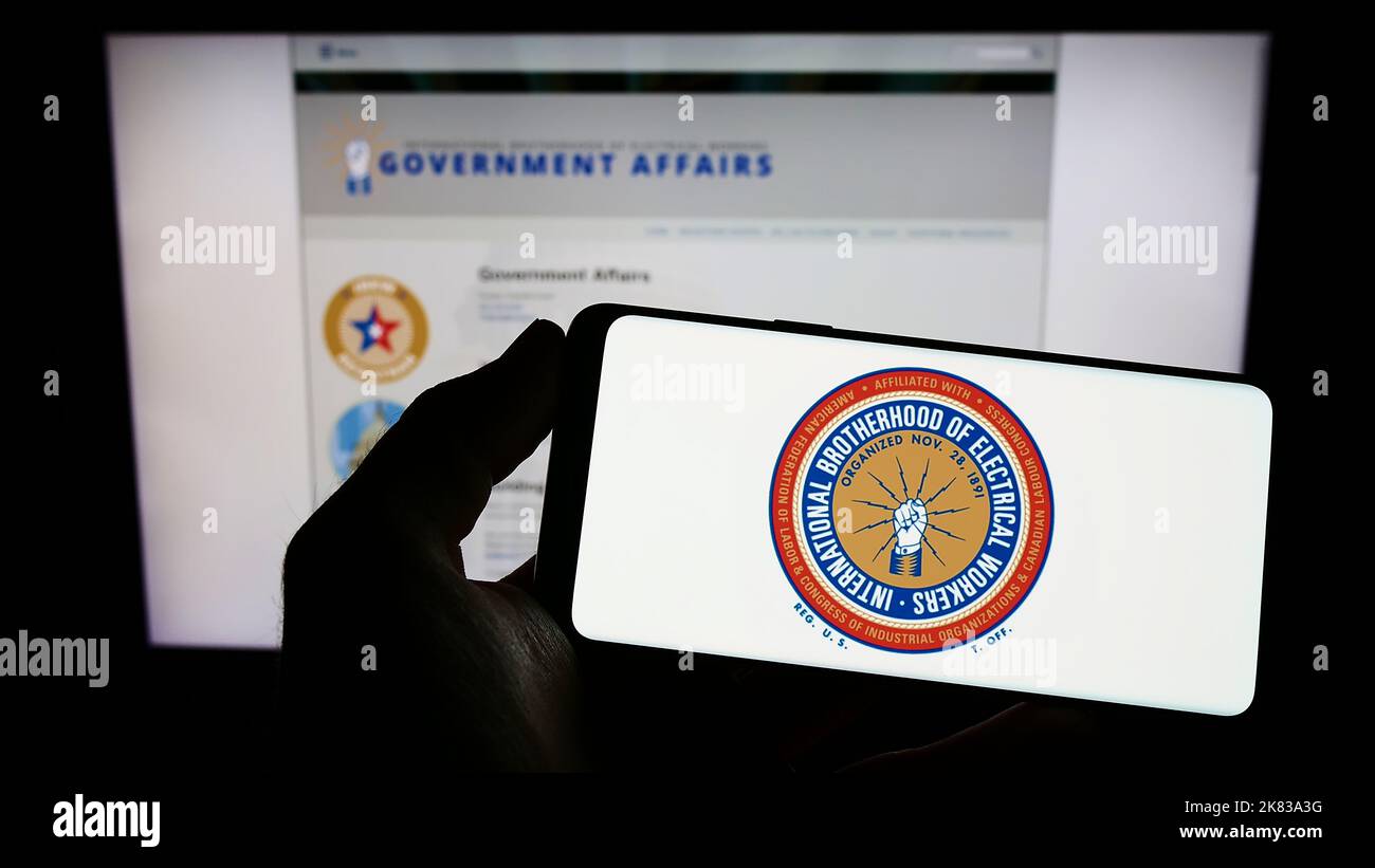 Persona che tiene lo smartphone con il logo del sindacato nordamericano IBEW sullo schermo di fronte al sito Web. Messa a fuoco sul display del telefono. Foto Stock