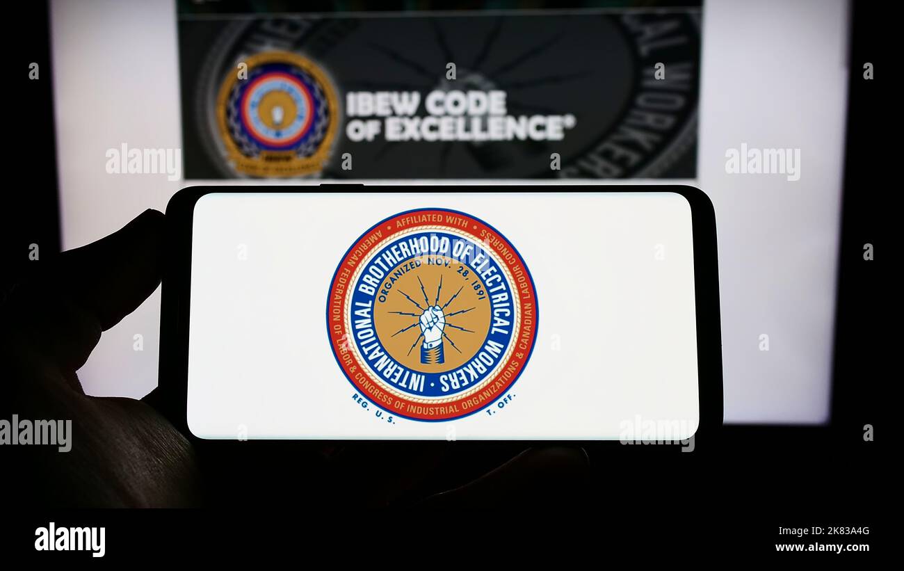 Persona che tiene il telefono cellulare con il logo del sindacato nordamericano IBEW sullo schermo davanti alla pagina web. Messa a fuoco sul display del telefono. Foto Stock