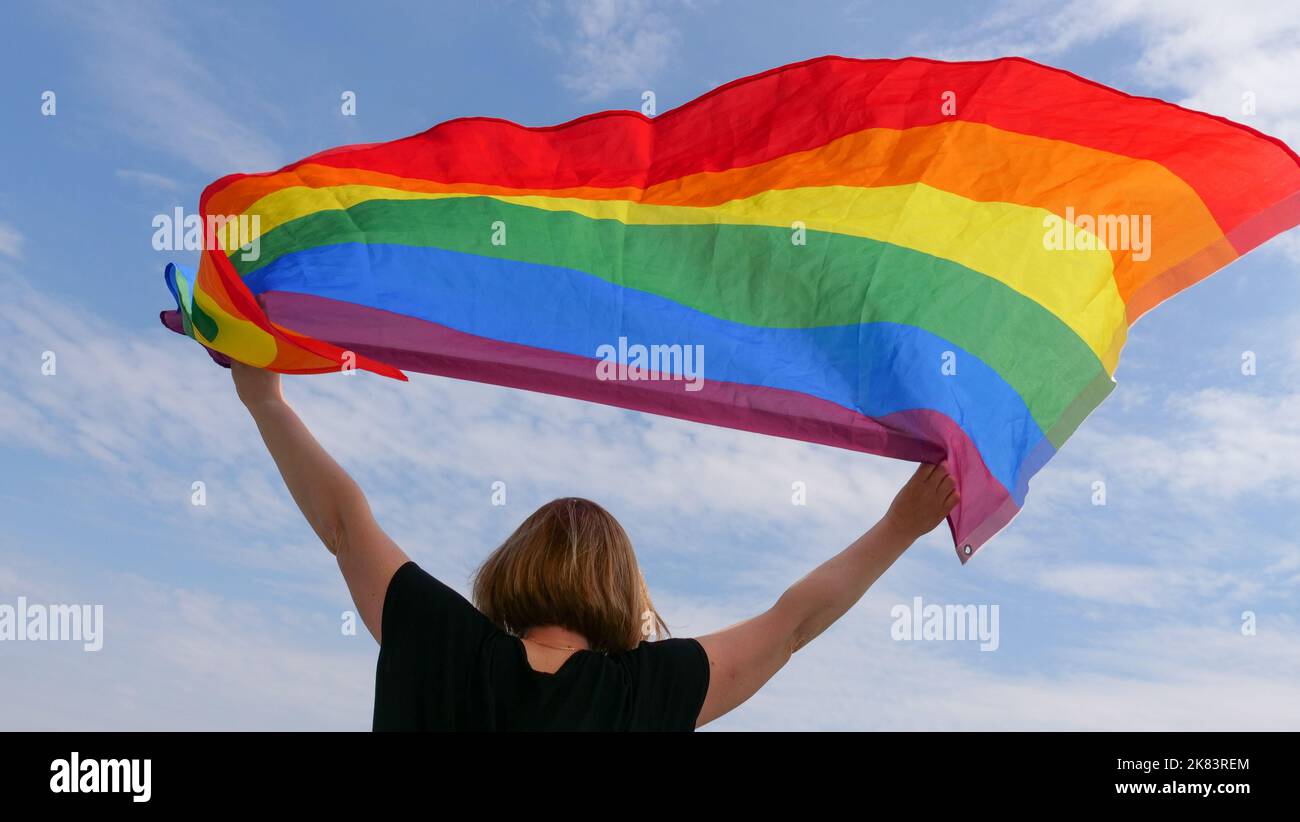 Bisessuale, ragazza, lesbica, donna, transgender, Omosessuale tenendo in mano un arcobaleno LGBT bandiera di identità di genere su sfondo cielo con le nuvole in una giornata di sole e celebrare una parata gay in mese di orgoglio Foto Stock