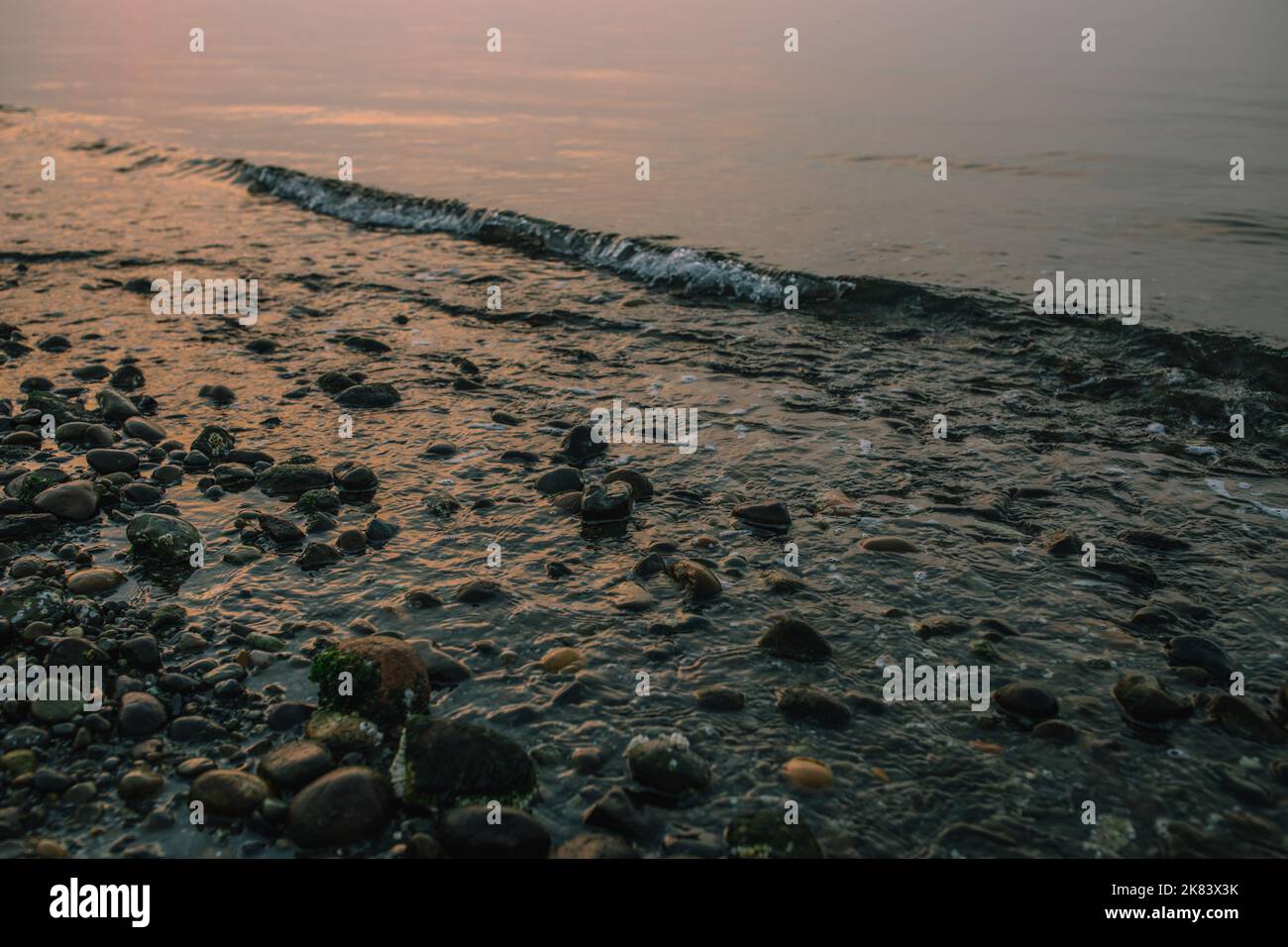 Spiaggia rocciosa del Pacifico nord-occidentale durante un tramonto fumoso Foto Stock