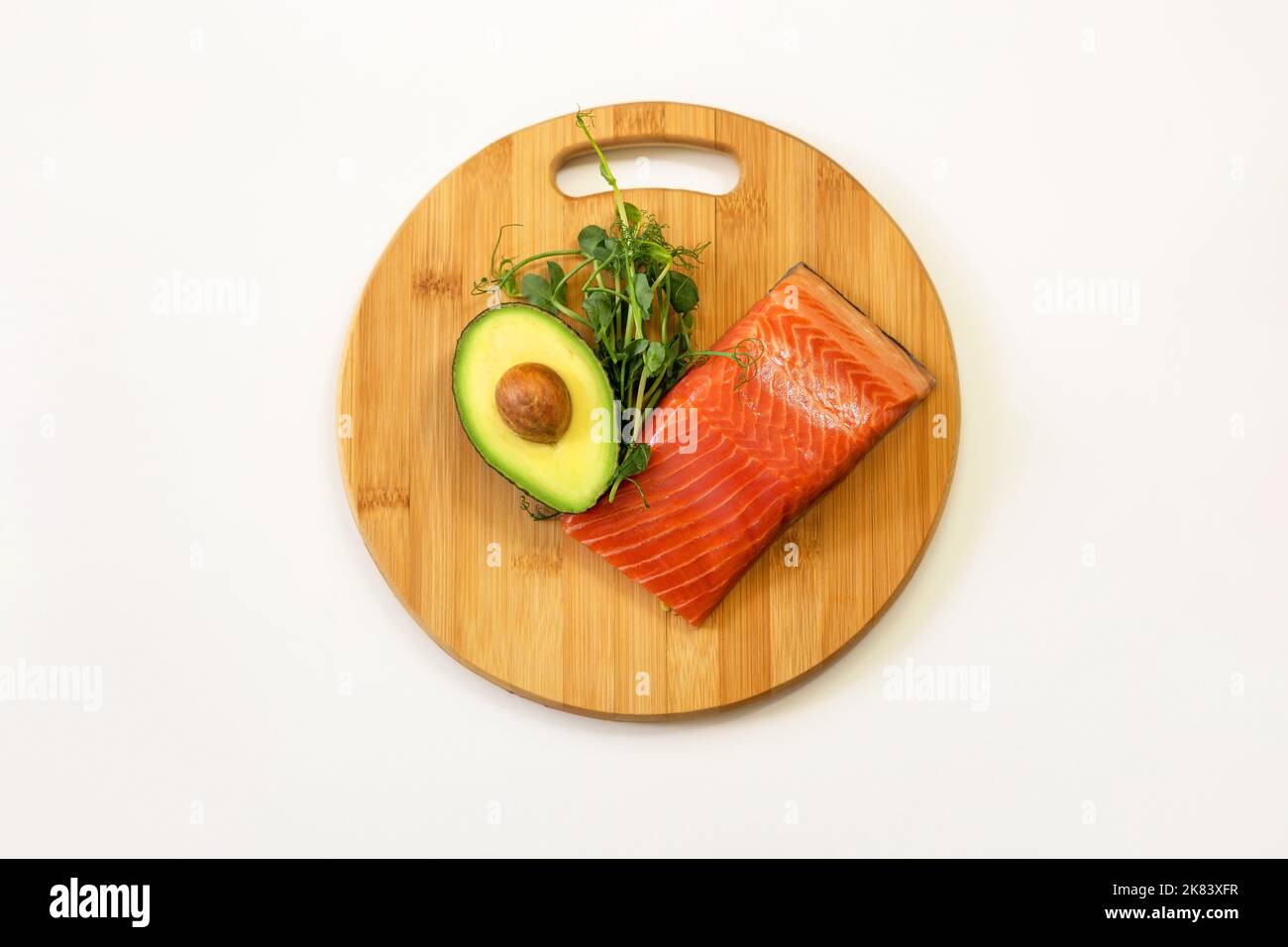Ingredienti di cibo sano. Pesce, avocado, micro piselli verdi germogli su un tagliere di legno. Ketogenic basso concetto di dieta dei carbs. Foto Stock