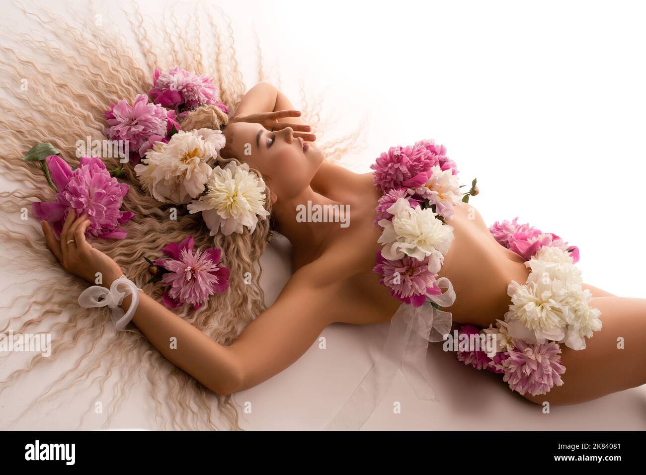 Donna nuda sensuale con fiori sul corpo sdraiato sul letto Foto Stock