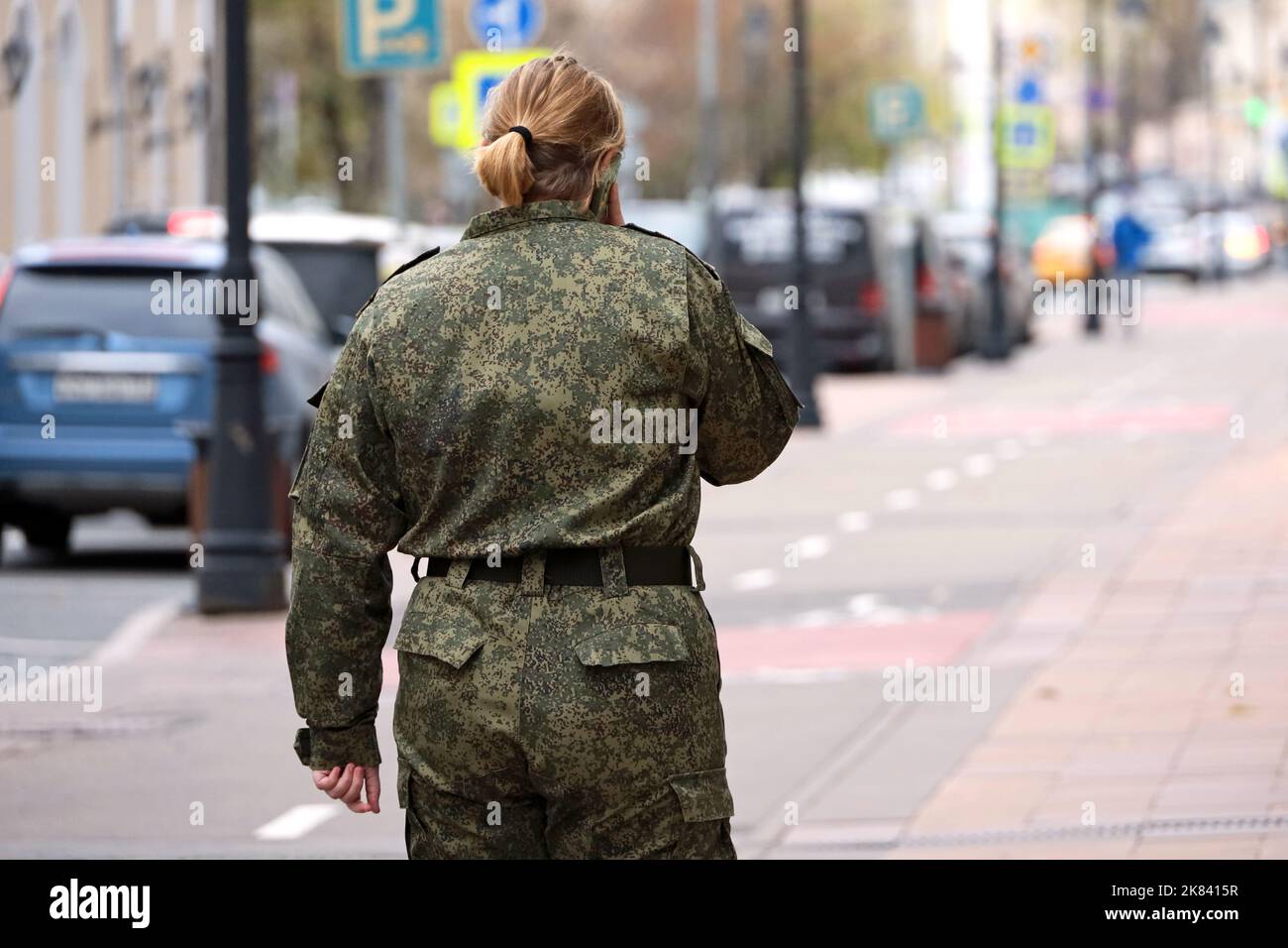 Donna in mimetizzazione militare che parla sul telefono cellulare mentre cammina per strada in autunno, vista posteriore Foto Stock