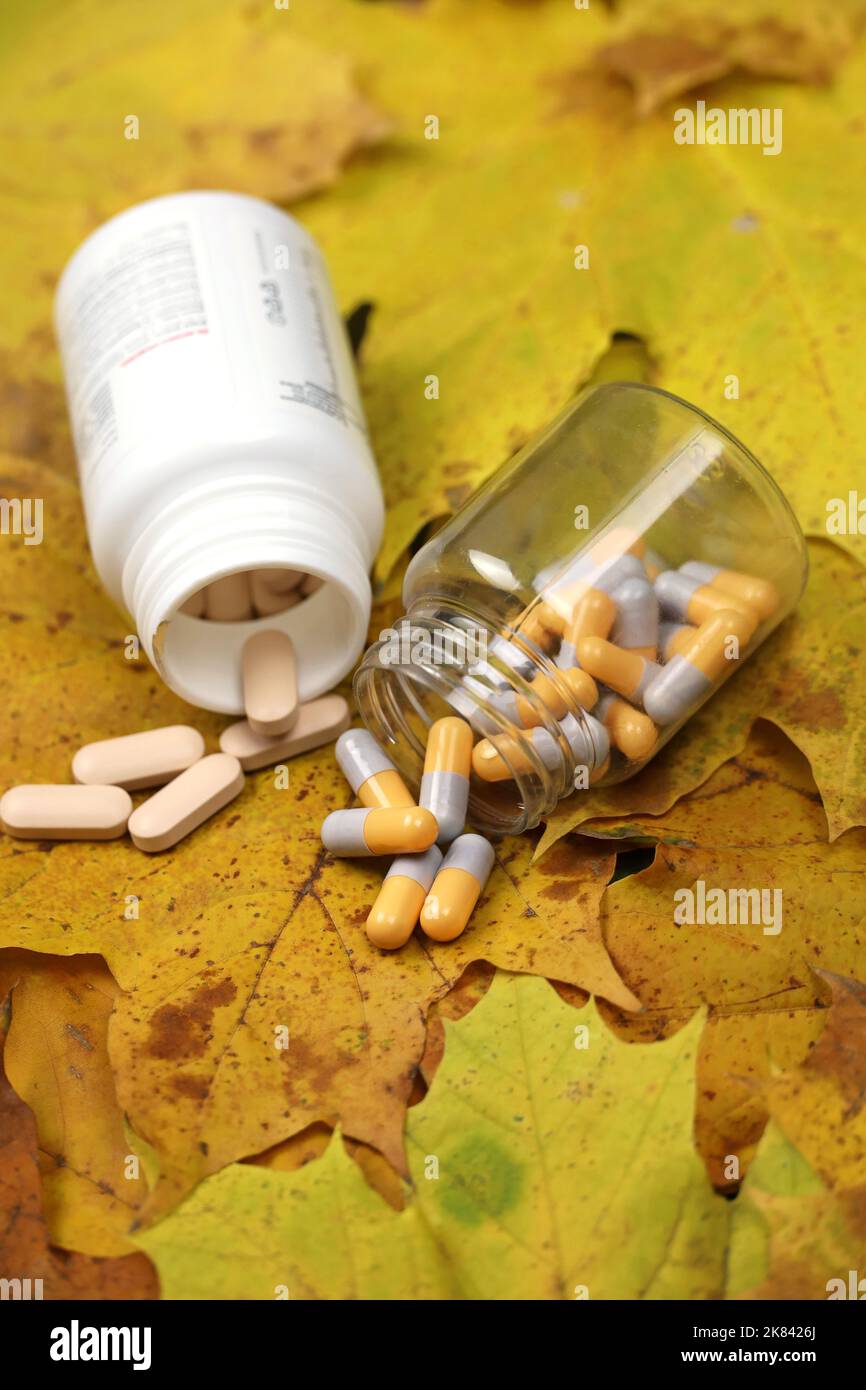 Pillole sulle foglie di acero autunnale, bottiglie con capsule sparse, colpo verticale. Farmacia, antidepressivi, vitamine per l'immunità nella stagione influenzale Foto Stock