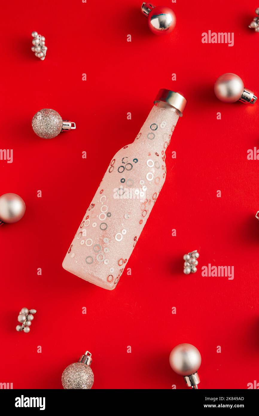 Lancio cerimoniale del concetto di Capodanno in bottiglia e Natale baubles su sfondo rosso. Idea di festa minima. Piano di giacitura, vista dall'alto. Foto Stock