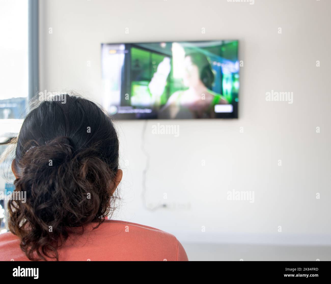 Il ritratto della donna da dietro guardando la tv sulla parete della stanza Foto Stock