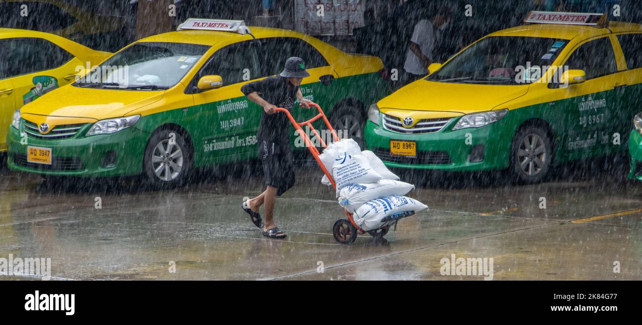 SAMUT PRAKAN, THAILANDIA, 26 2022 SETTEMBRE, Un portiere che spinge un carrello con un carico di sacchi nella strada della pioggia Foto Stock