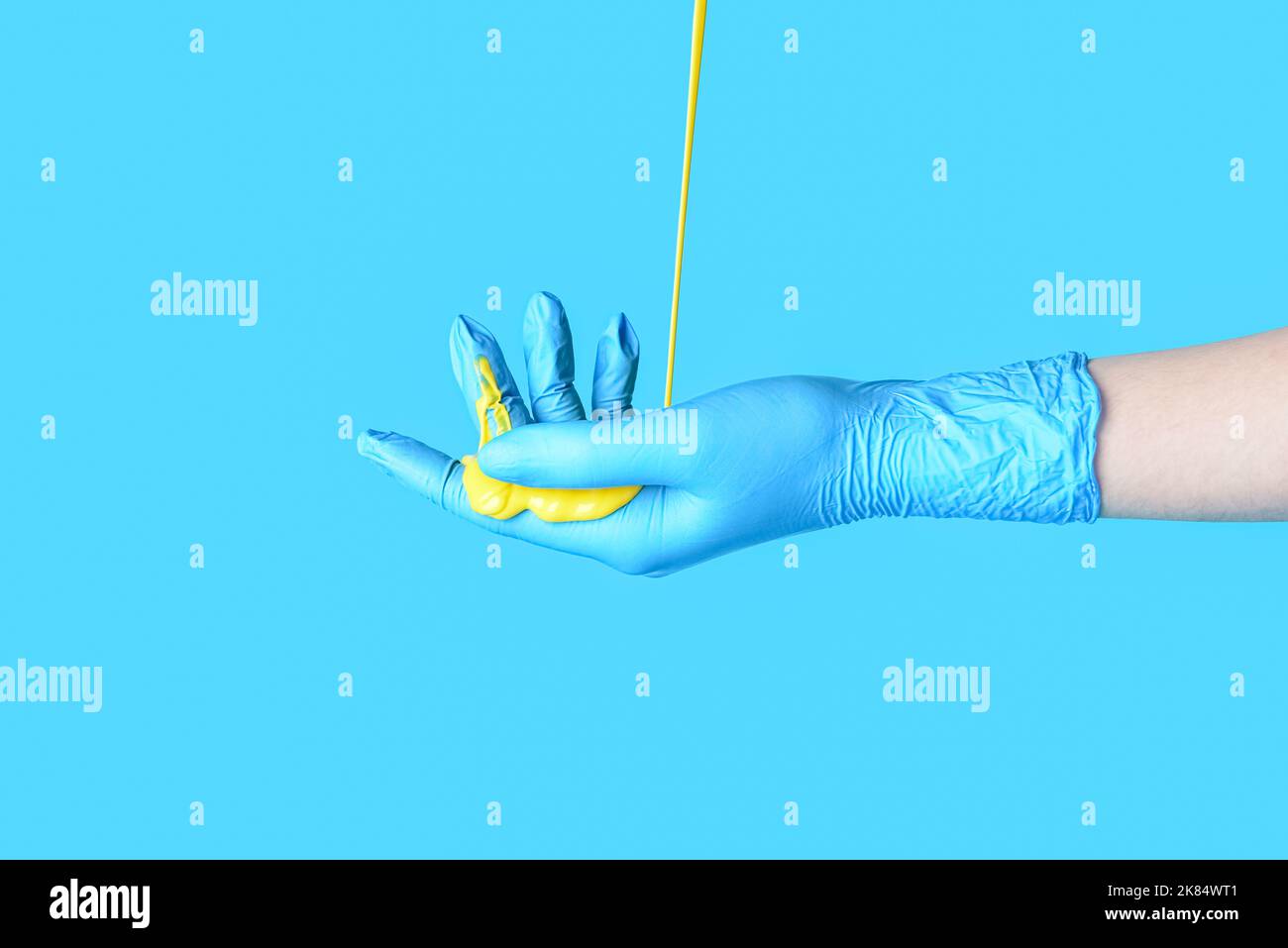 Vernice che si riversano sulla mano del medico femminile in guanto medico contro sfondo colorato Foto Stock