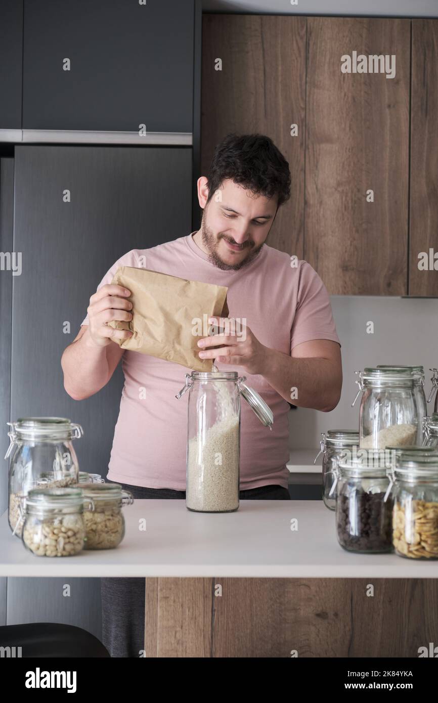 Giovane uomo latino che riempie un vaso con riso a grana tonda da un sacchetto di carta. Foto Stock